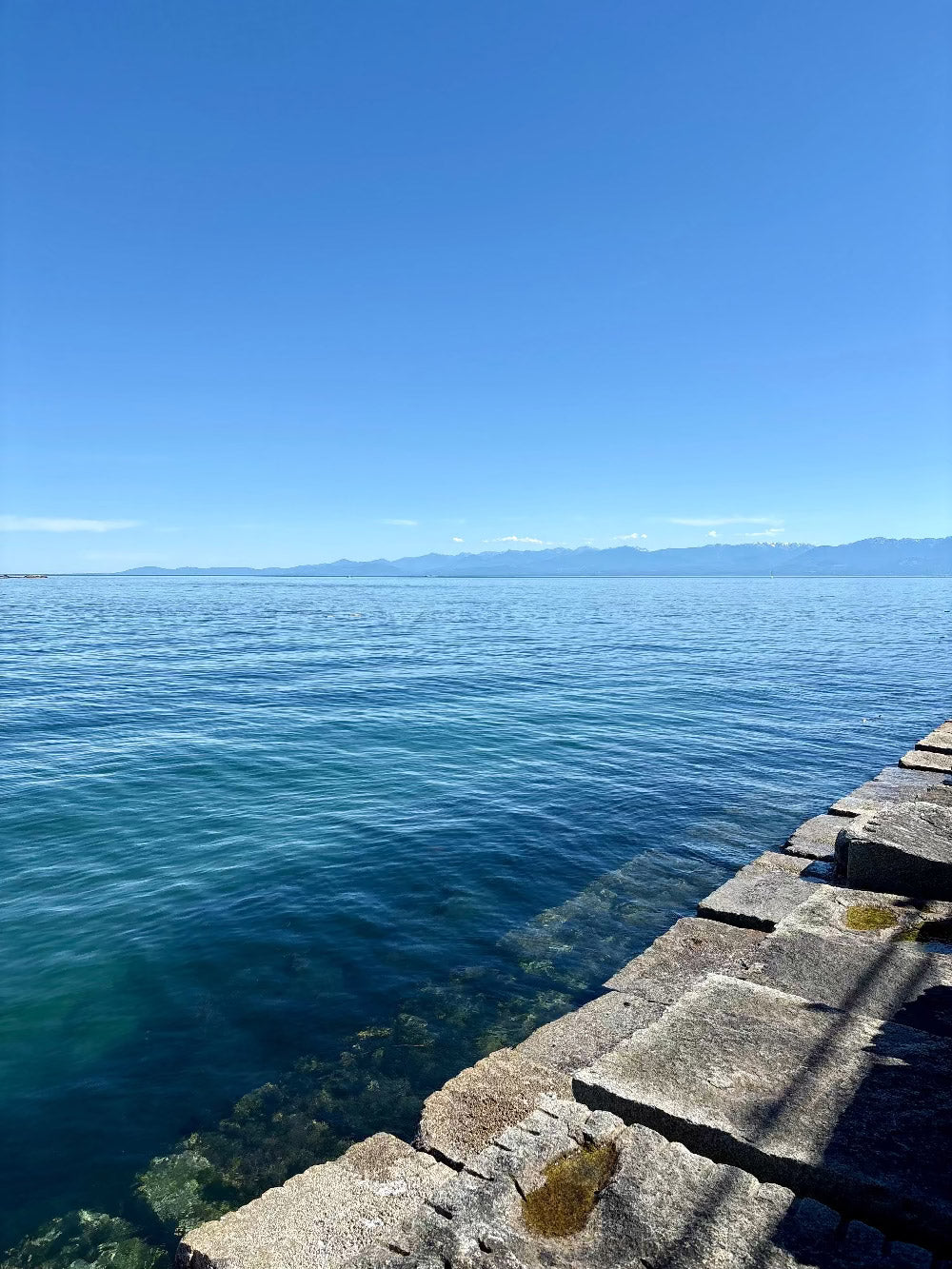 Stone pier extending into a calm blue body of water under a clear sky in Victoria, BC on Vancouver Island