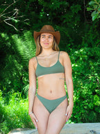 Woman wearing a green bikini and brown hat in a forest setting on a beach in Victoria, BC