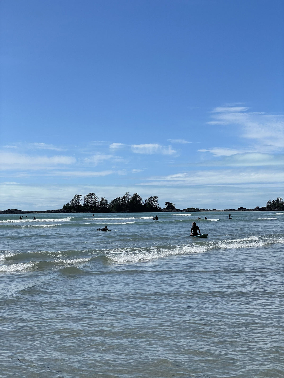 People surfing in a body of water with a clear blue sky above in Tofino, BC on Vancouver Island
