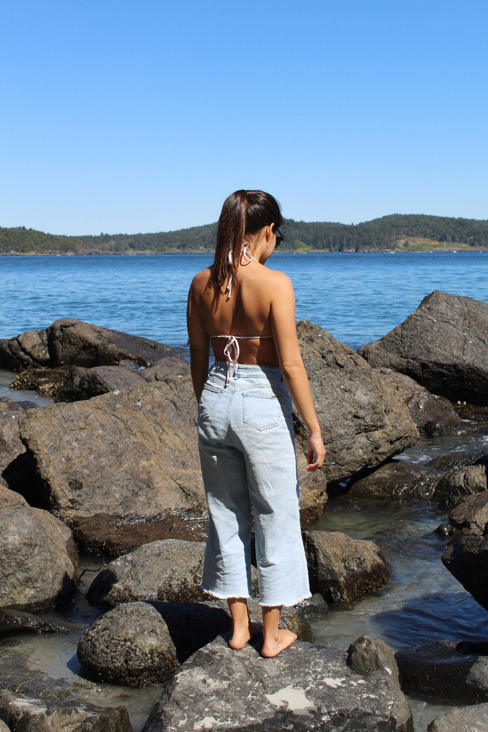 Woman standing on rocks by a body of water with a clear blue sky on Vancouver Island